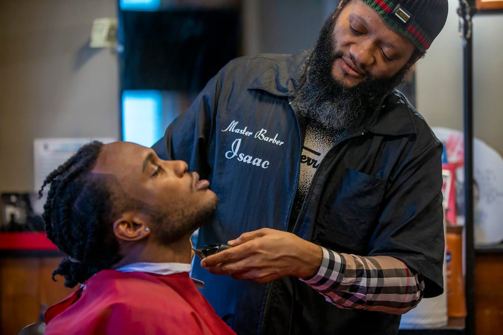 Master barber Issac Genty trims the beard of his son Bright, who is training to become a barber himself at Head Lines Unisex Barber Shop in Cambridge.
