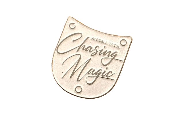 A sparkly white pin in the shape of a metal shoe tap that says “Ayodele Casel: Chasing Magic”.