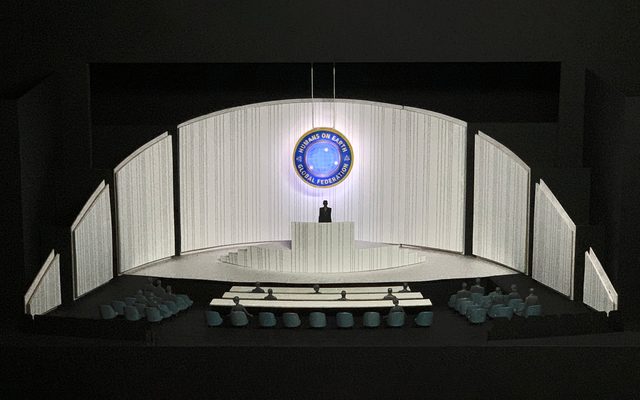 A model of the Ocean Filibuster set: a patterned white stage with a podium against a black background.