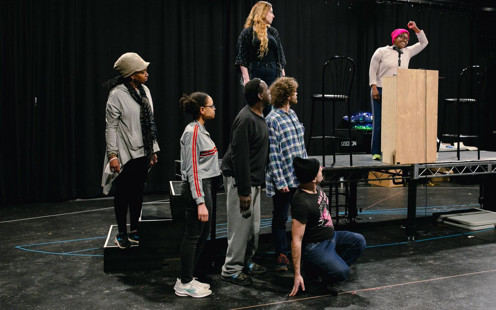 The Ocean Choir looks on as Jennifer Kidwell orates from a lectern in rehearsal.