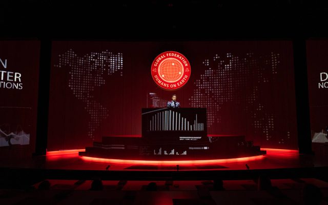 Jennifer Kidwell at the podium and the staged bathed in red.