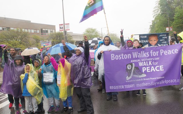 Adults and children march down a rainy street with a banner that reads, “Boston Walks for Peace.“