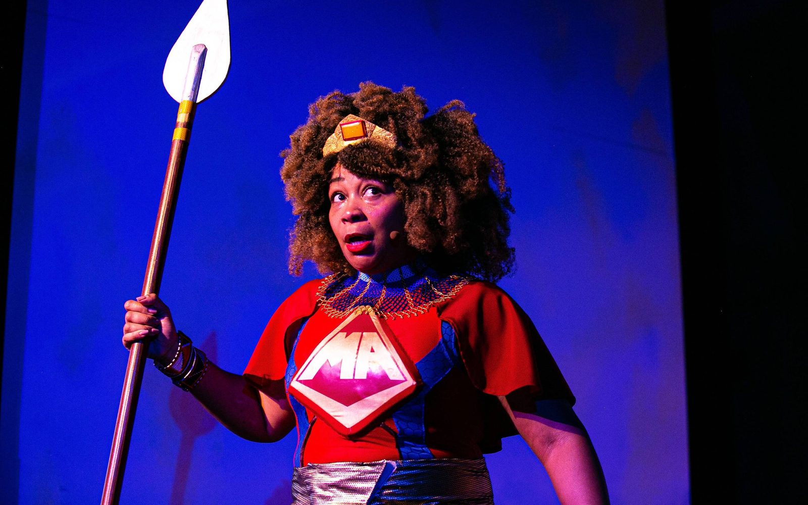 Ramona Lisa Alexander as the Maasai Angel and holding a spear in Black Super Hero Magic Mama.