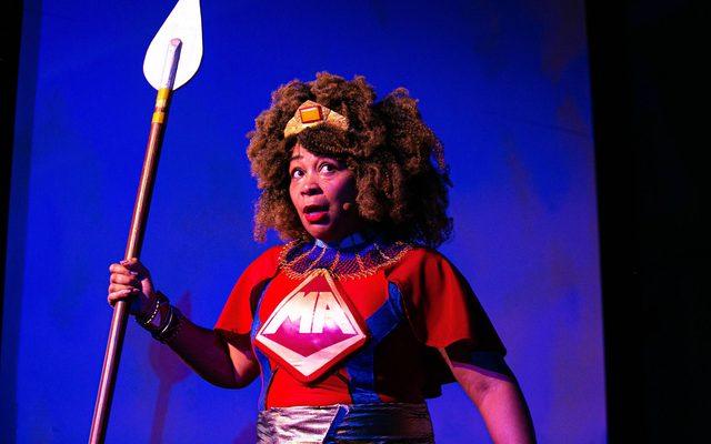 Ramona Lisa Alexander as the Maasai Angel and holding a spear in Black Super Hero Magic Mama.