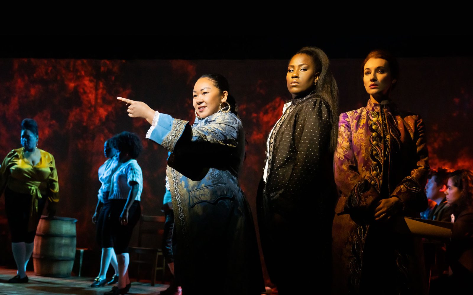 Sara Porkalob, Crystal Lucas-Perry, and Elizabeth A. Davis stand in a group in front of members of the company.