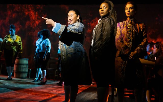 Sara Porkalob, Crystal Lucas-Perry, and Elizabeth A. Davis stand in a group in front of members of the company.