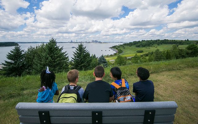 Five kids sitting on a bench take in the view of Boston from Spectacle Island.