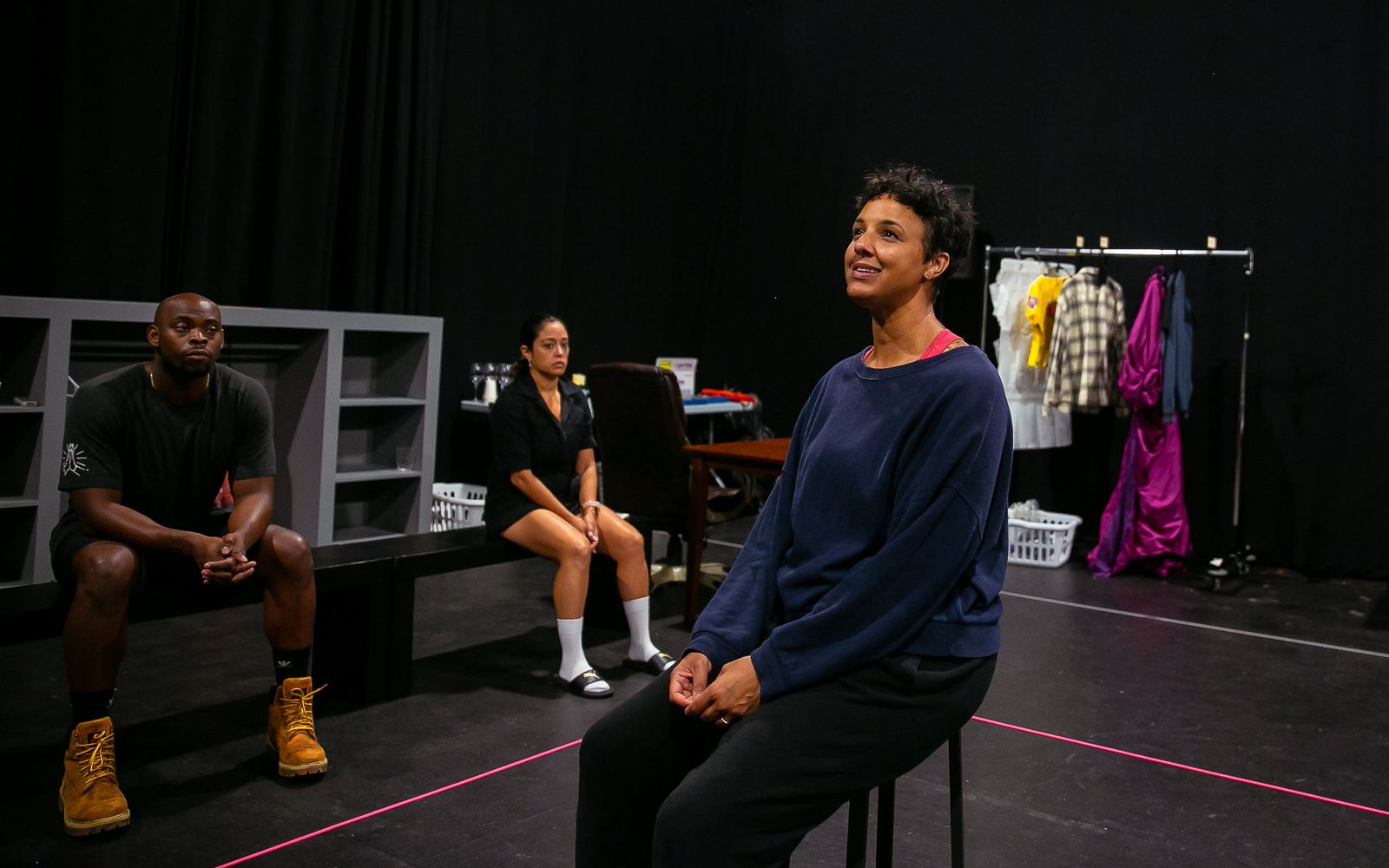 Tiffany Rachelle Stewart on a stool while Wesley T. Jones and Elena Hurst look on in rehearsal.
