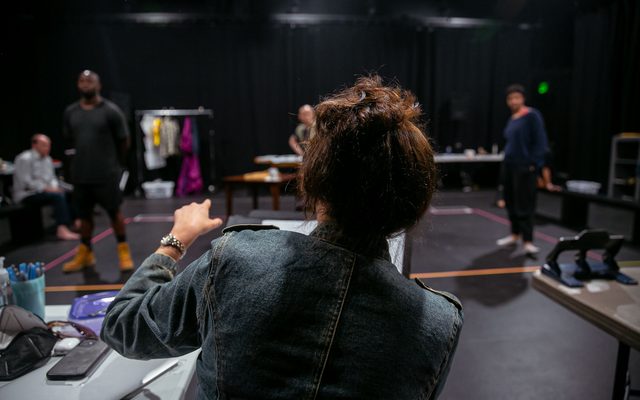 The back of Director Taibi Magar as she works with the actors in rehearsal.