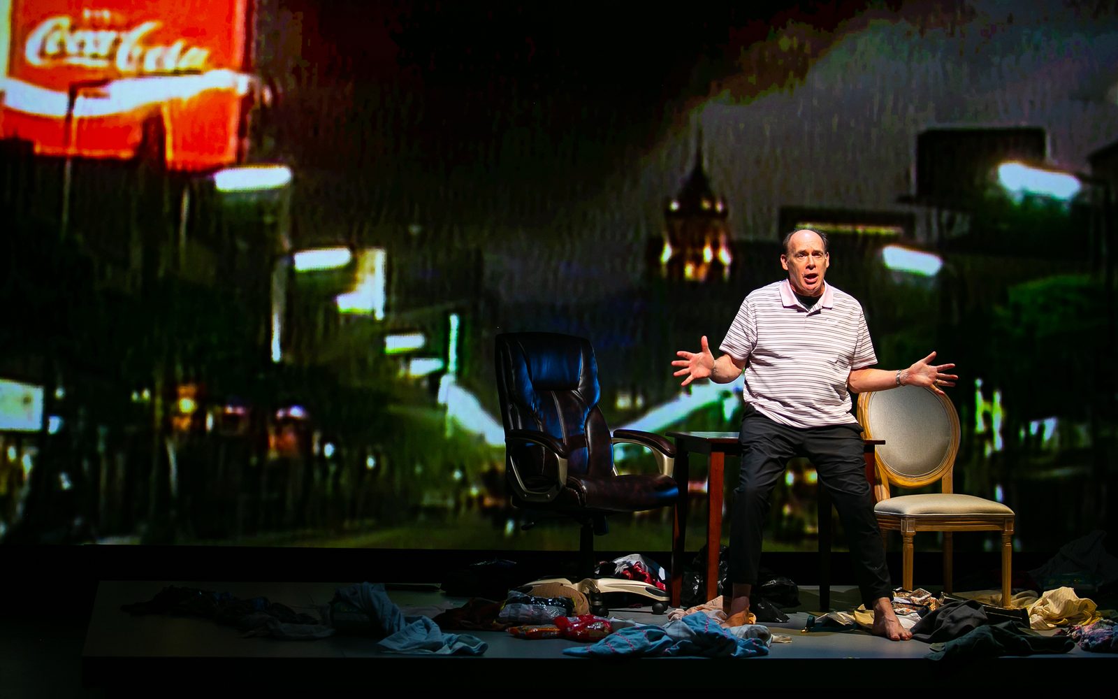 Carl Palmer in a striped polo leaning on a table in front of a wall of a shopping street at night lit by a red Coca-Cola sign.