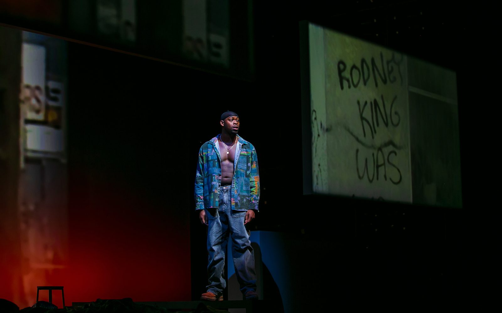 Wesley T. Jones in a patched denim coat, jeans, and a durag spotlit on a dark stage.