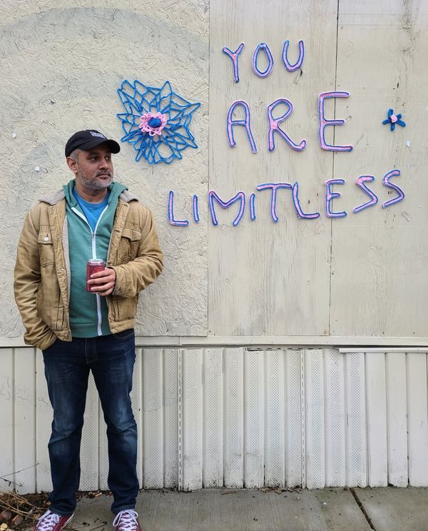 Rajesh Bose standing in front of a wall decoration that says, “You are limitless”.