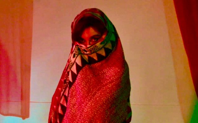 A young woman wrapped in a red shawl reveals only her eyes.