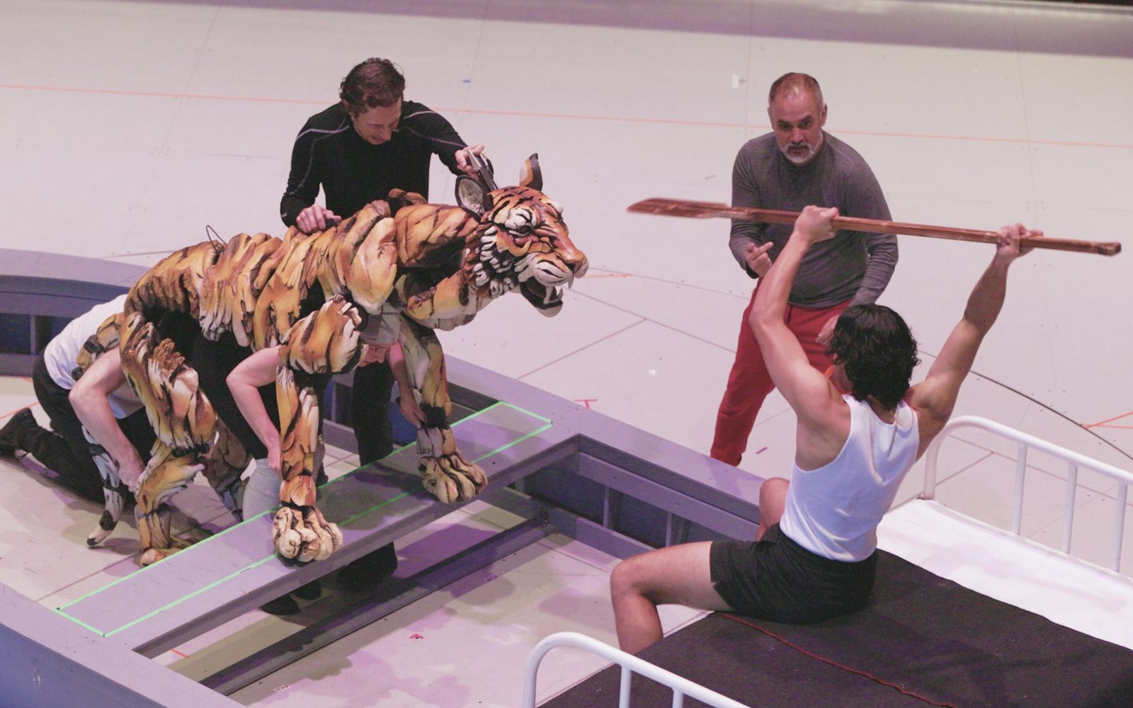 Adi Dixit raises an oar above his head as puppeteers manipulate a tiger puppet towards him.