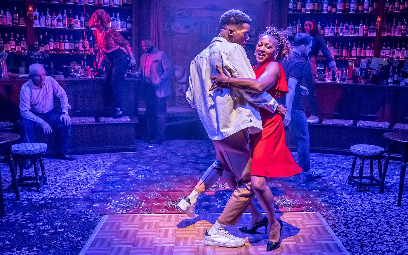 Troy Glasgow in a denim jacket and Clare Perkins in a red dress embrace each other in a close dance.