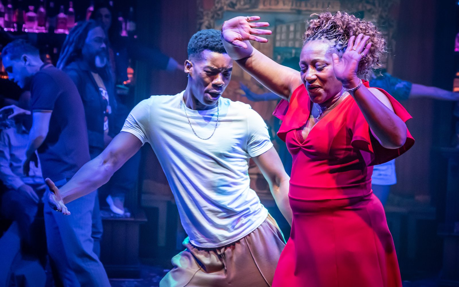Troy Glasgow in a white T-shirt and thin chain dances with Clare Perkins in a red dress.