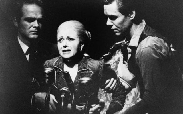 Elaine Paige as Eva Perón making a speech into several microphones.