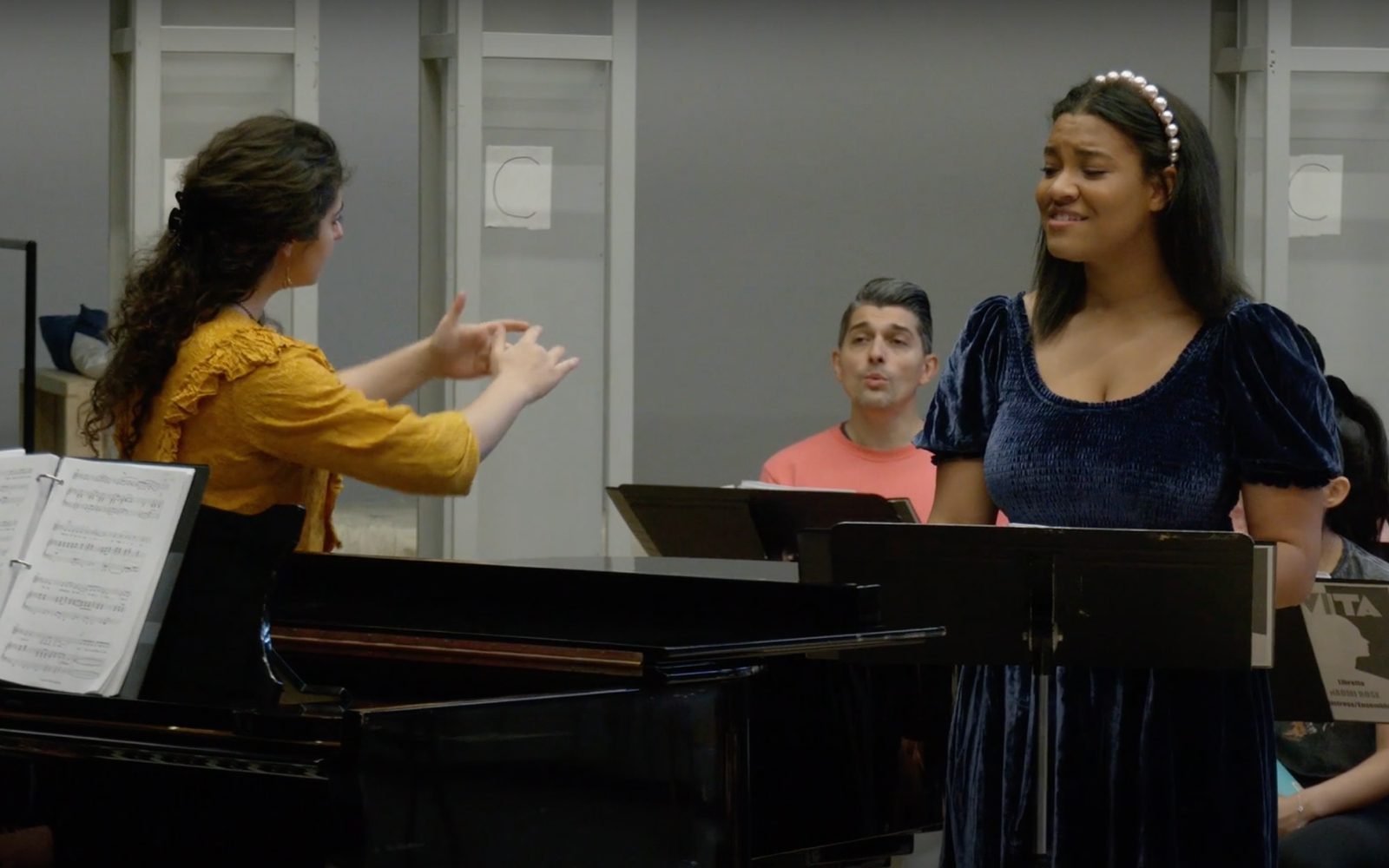 Mona Seyed-Bolorforosh conducts the ensemble, including Julian Alvarez, while Shereen Pimentel sings at a piano.