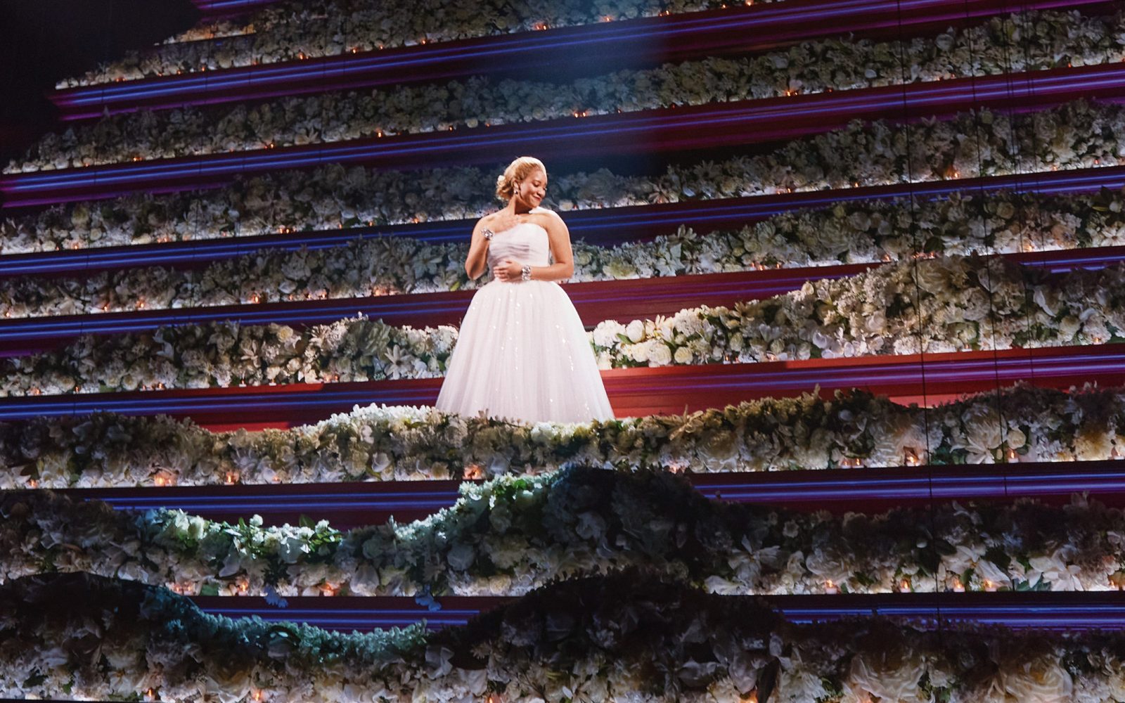 Shereen Pimentel as Eva standing on steps covered in white flowers.