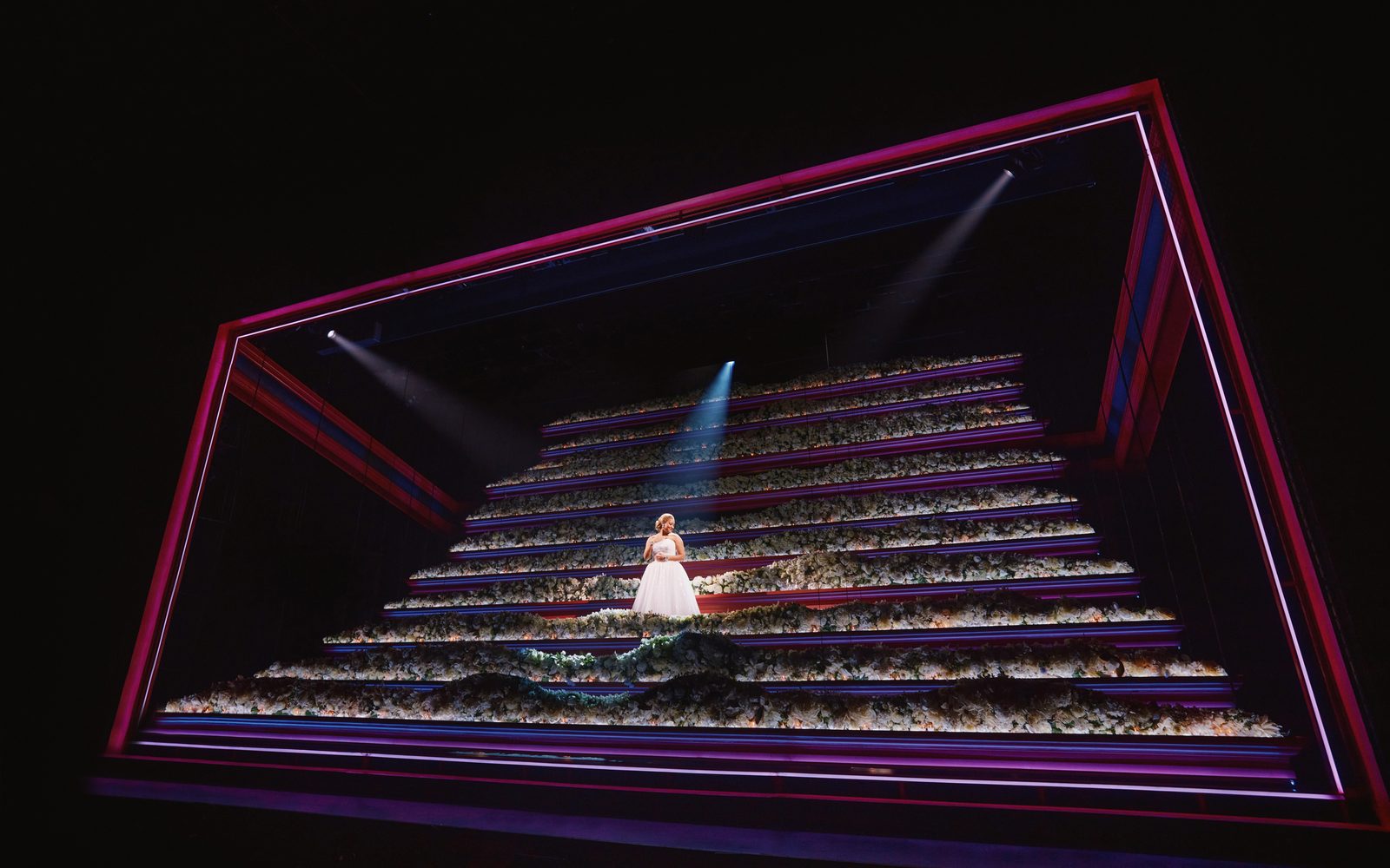 Shereen Pimentel as Eva standing on steps covered in white flowers.