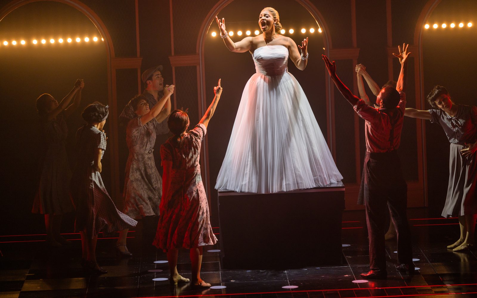 Shereen Pimentel (Eva) sings on a pedestal in a white dress, while company members watch with their arms raised.