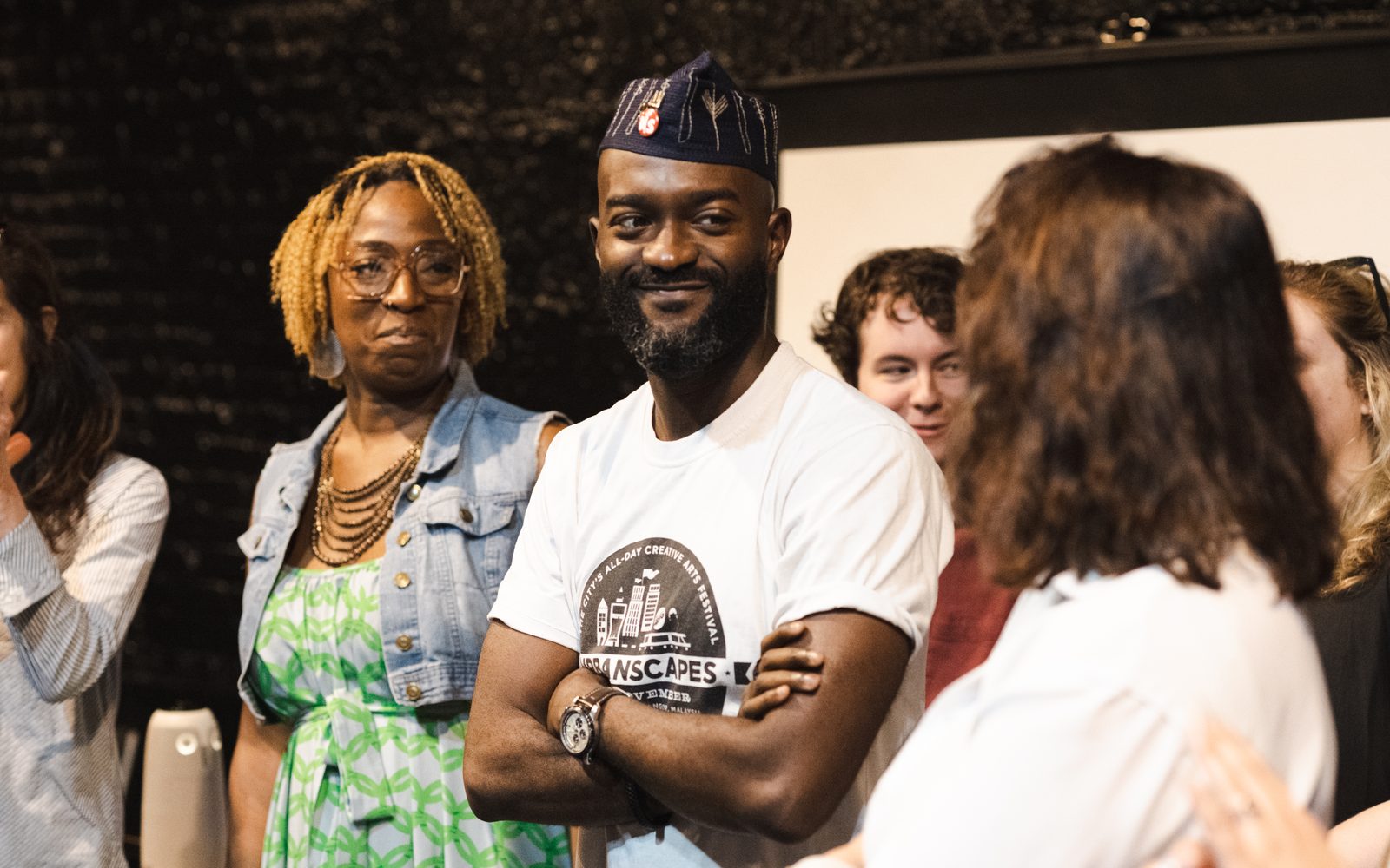 Inua Ellams smiles while standing amidst a group of people.