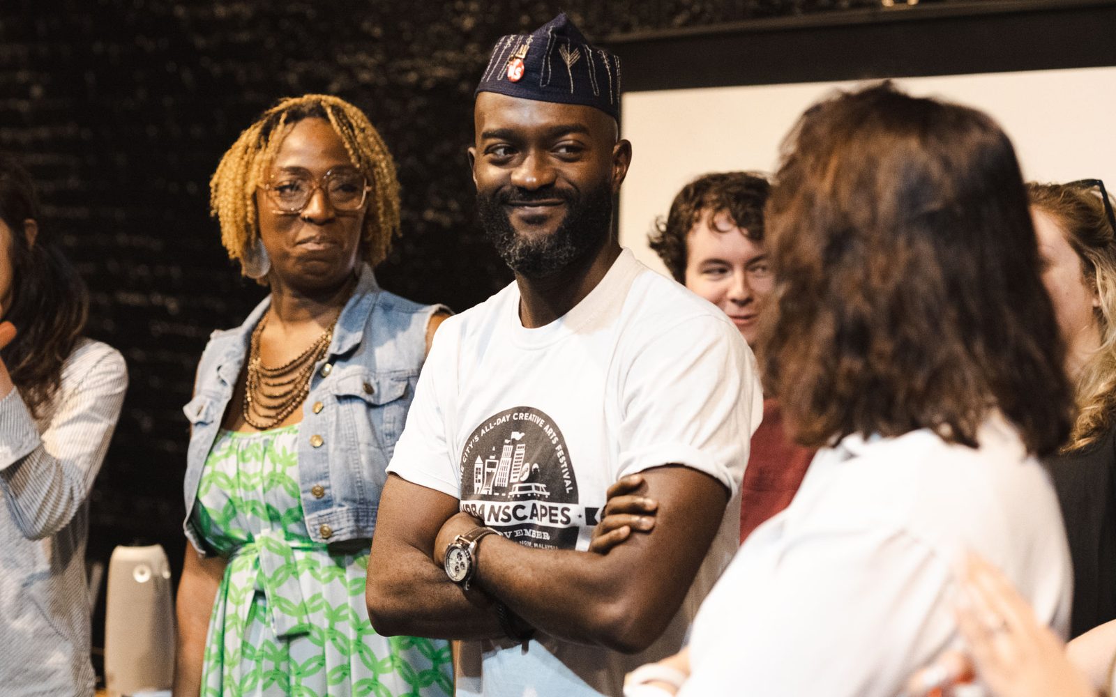 Inua Ellams smiles while standing amidst a group of people.