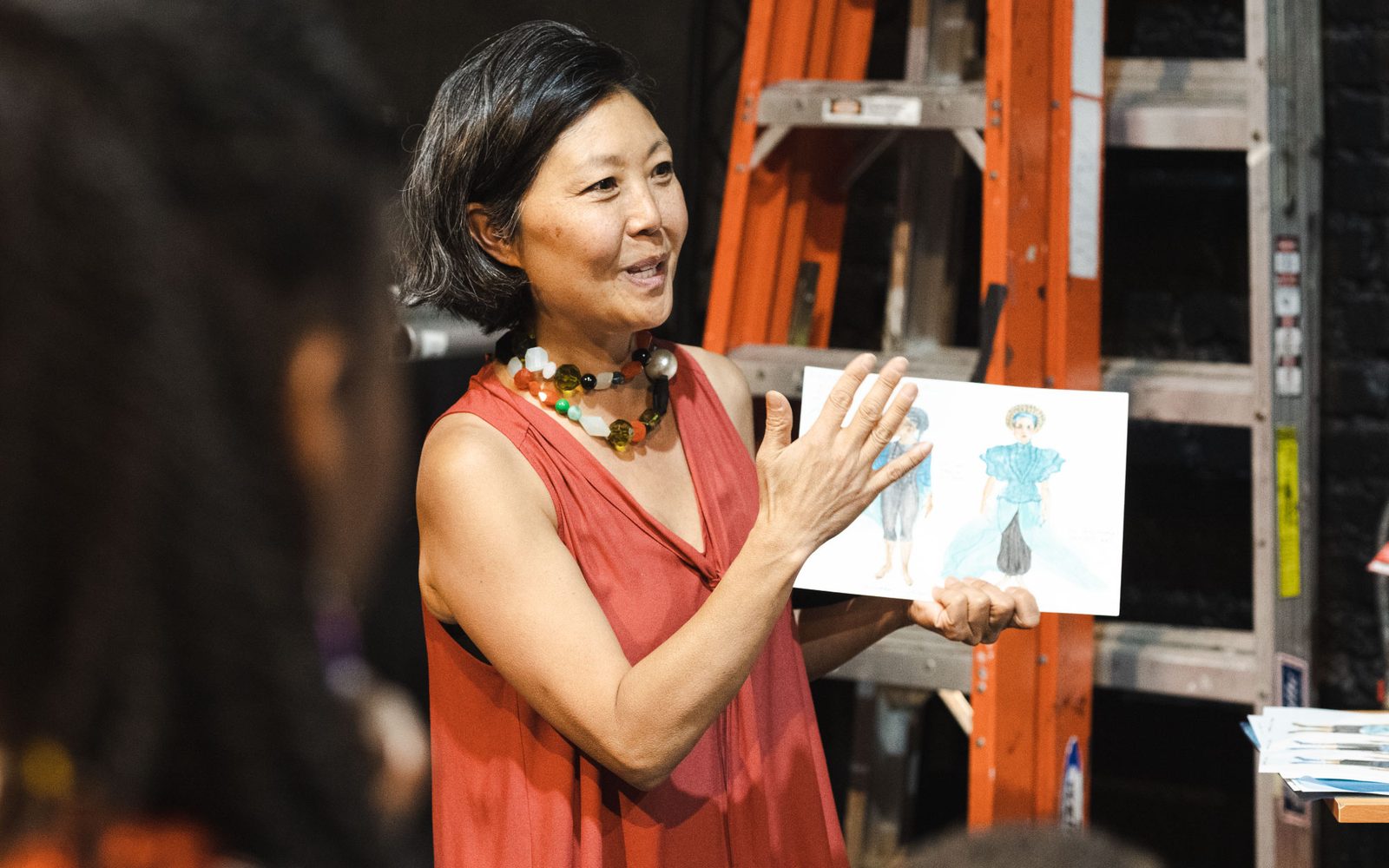 Linda Cho talks with a costume design in her hand.