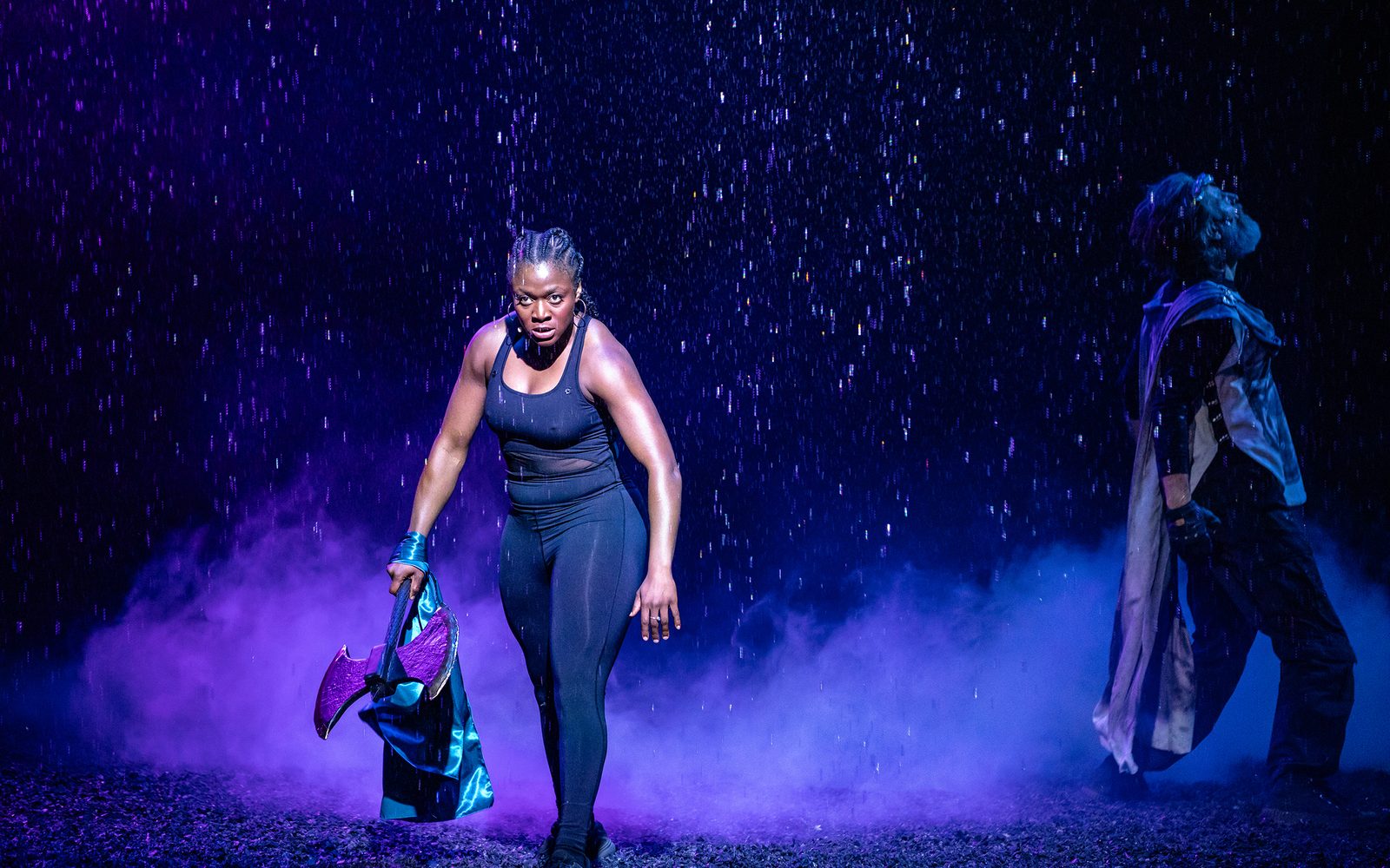 Jennifer Mogbock holds an axe and Michael Lauren staggers to the side as rain falls around them.