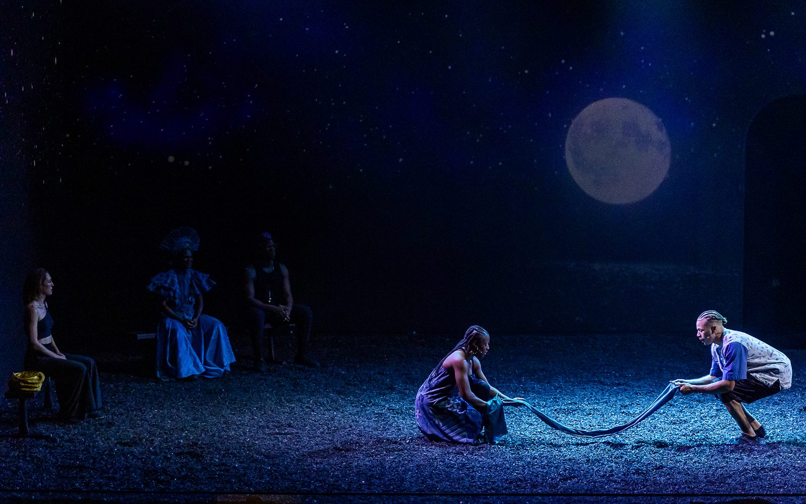 Jennifer Mogbock and Mister Fitzgerald crouch to pick up a long piece of fabric as Kelley Curran, Patrice Johnson Chevannes, and Jason Bowen sit to the side watching them.