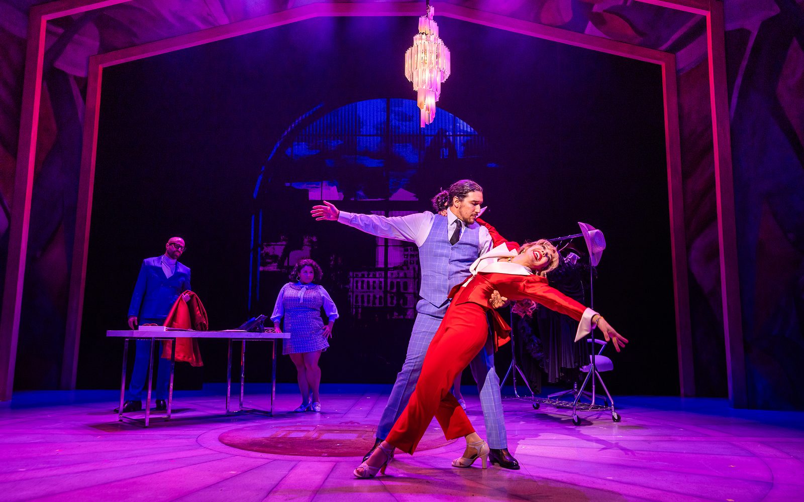 Christopher M. Ramirez dips Yvette González-Nacer while dancing in the the office, while Arusi Santi and Elisa Galindez watch from the background.