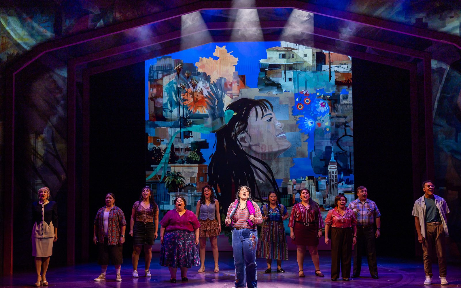 The company gathers singing in front of a mural of Ana's face and Boyle Heights buildings projected onto the background.