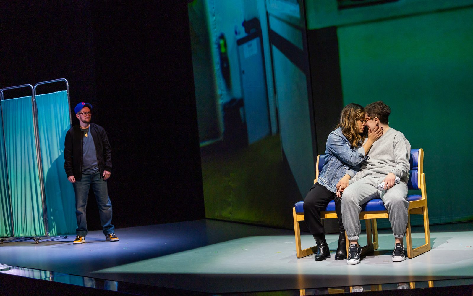 Elena Hurst leans in close to Stacey Raymond on a bench, while Carl looks on from the side.