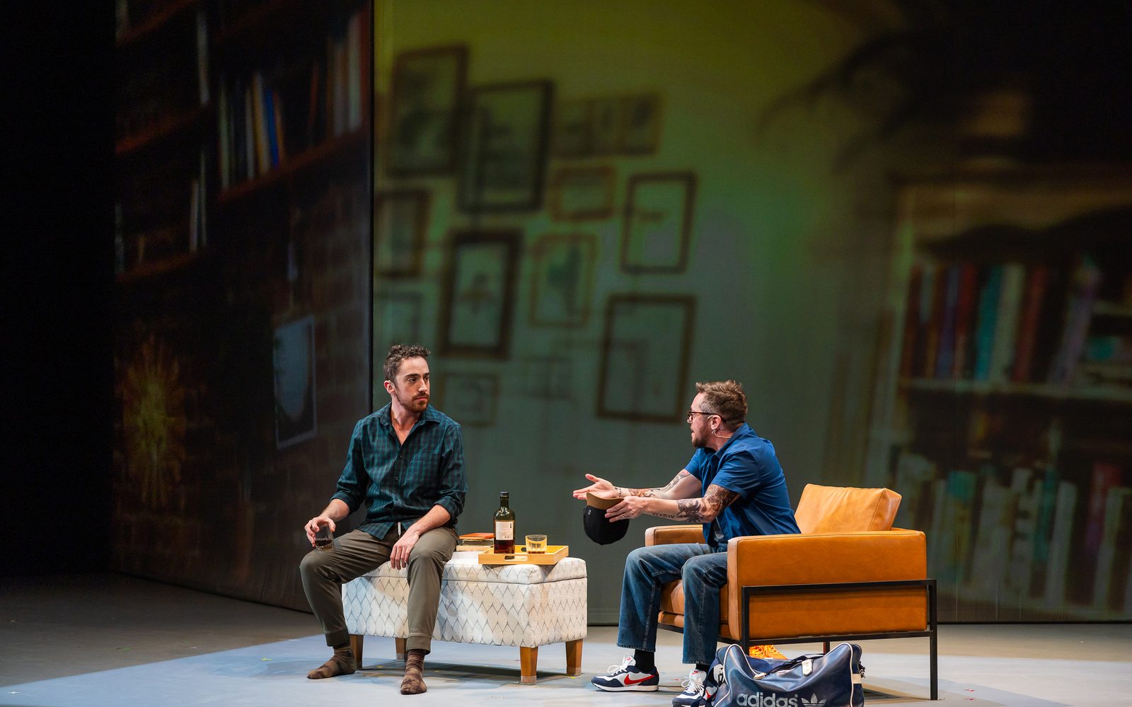 Cody Sloan sits on an ottoman with a glass in hand as Petey Gibson sits next to him in a chair gesticulating.