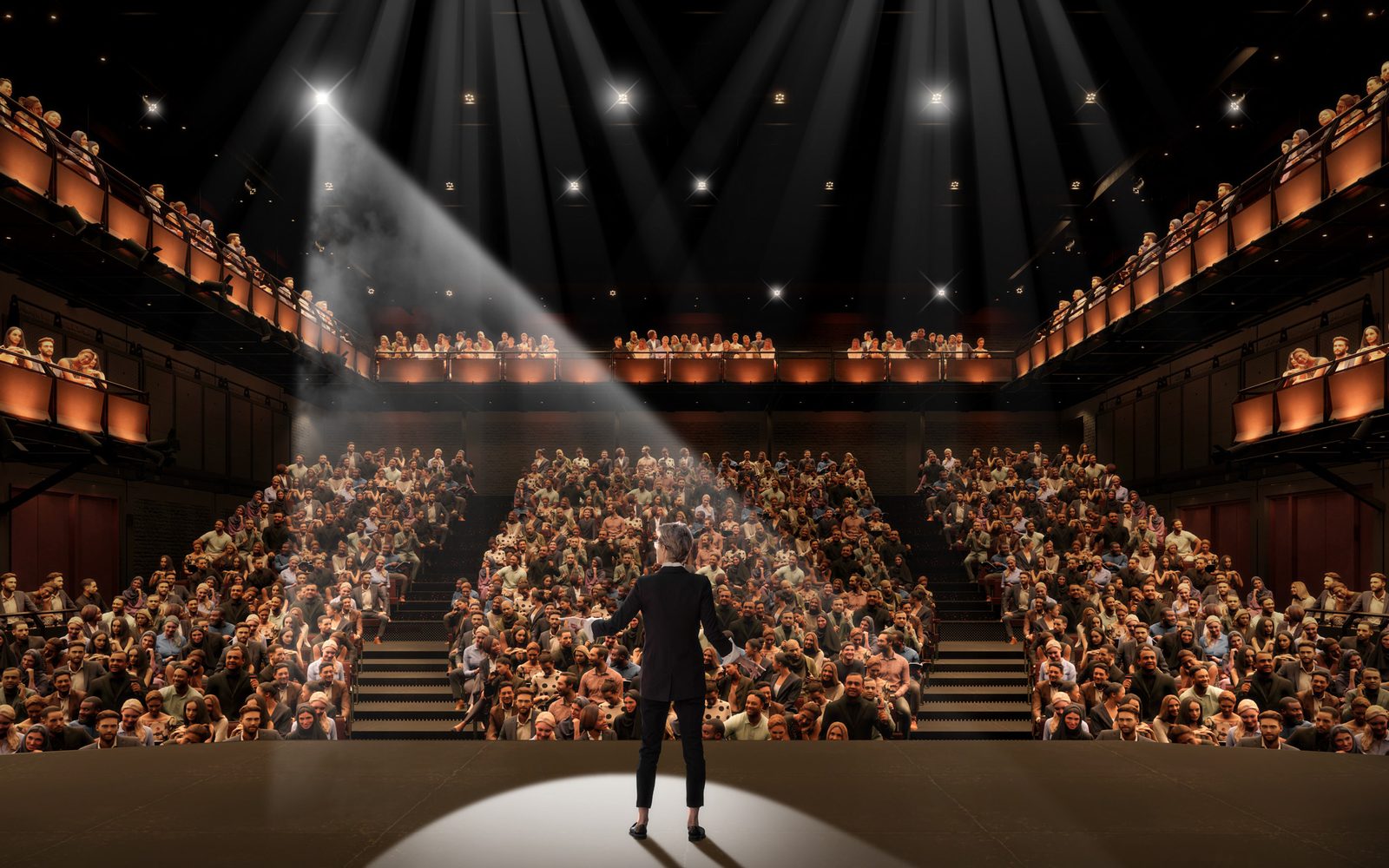 Looking out from the West Stage, with a performer spotlit onstage, people sitting in the orchestra level, boxes on either side, and a balcony.
