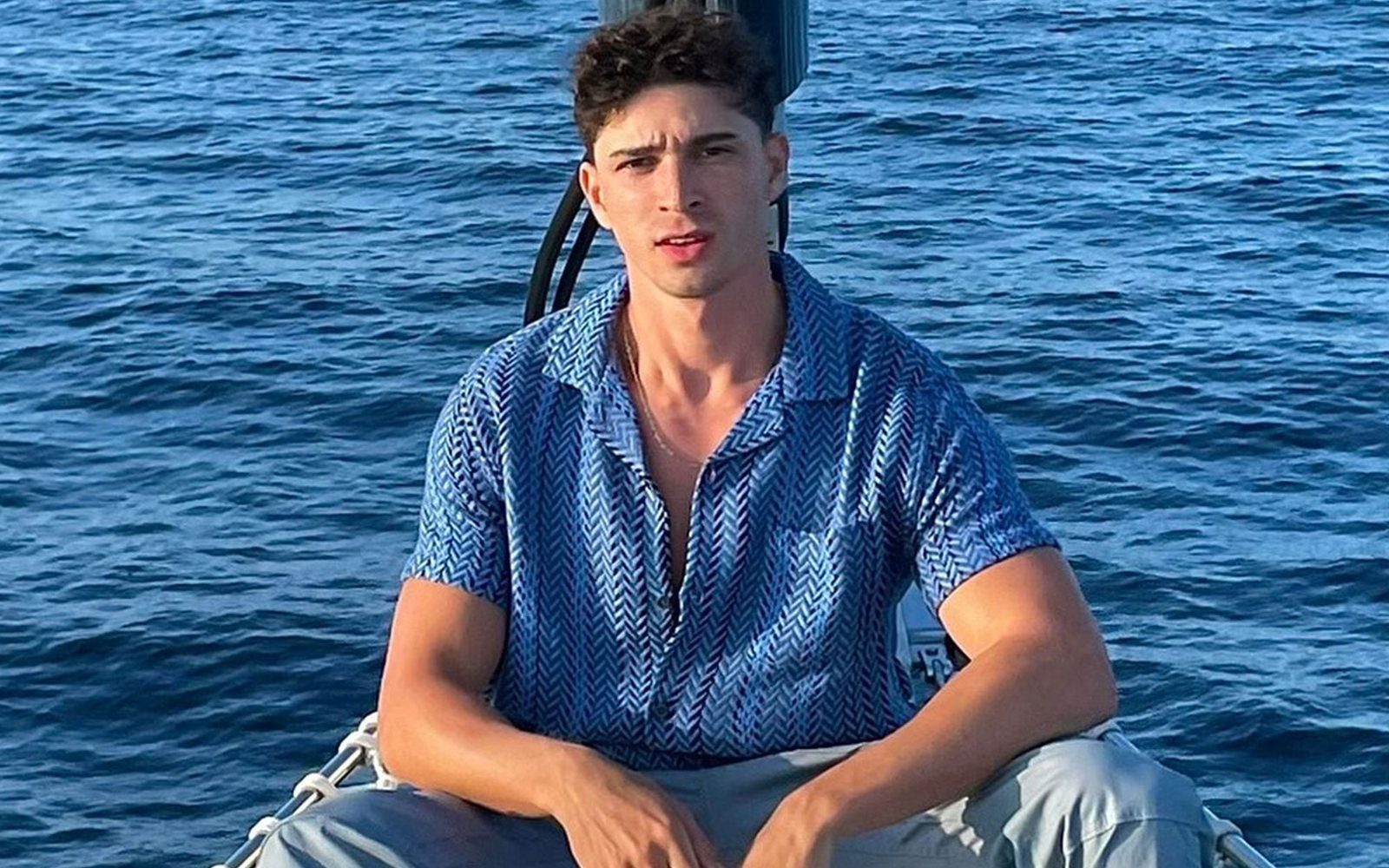 Isaac Powell in a blue herringbone-patterned shirt sitting on a boat in the water.