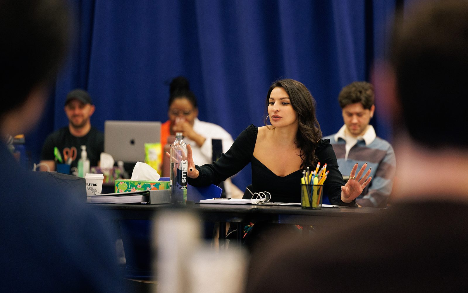 Seated at a table, Martyna Majok gesticulates while speaking to other people.