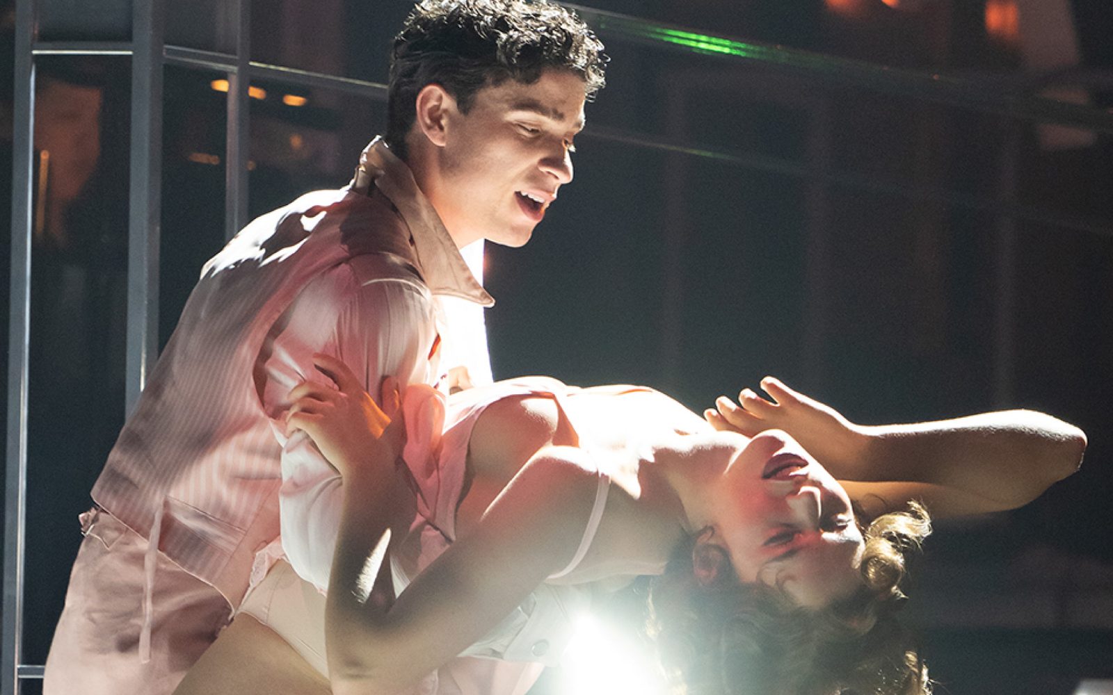 Isaac Powell dips Charlotte MacInnes on a curved staircase, with a light reflecting through the arch of her back.