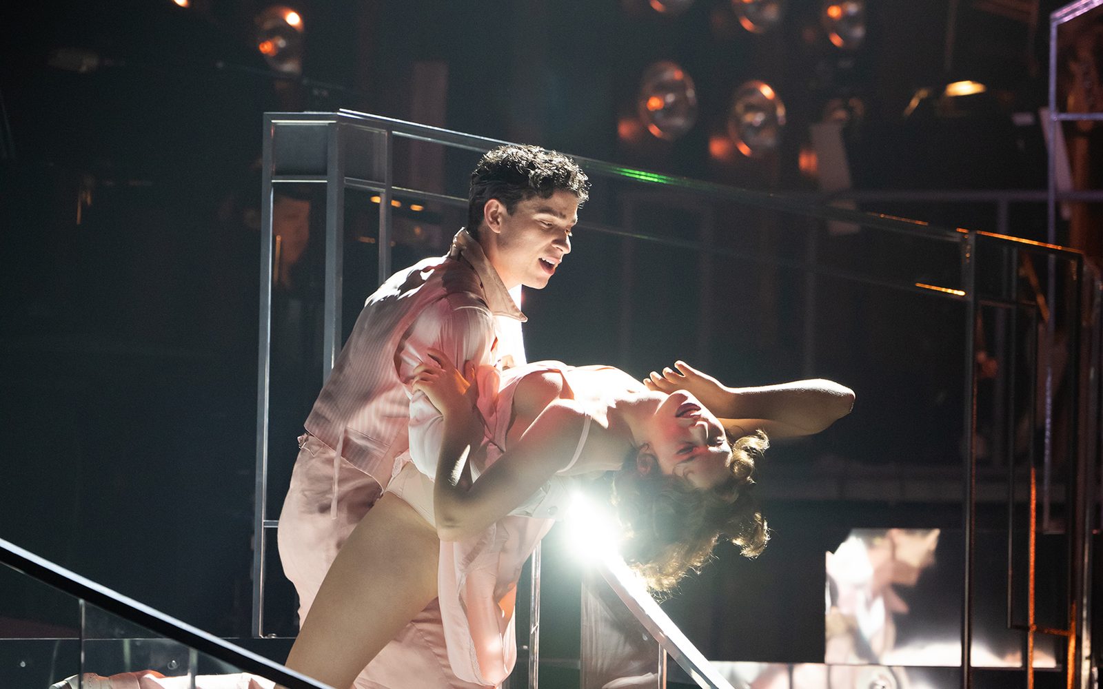 Isaac Powell dips Charlotte MacInnes on a curved staircase, with a light reflecting through the arch of her back.