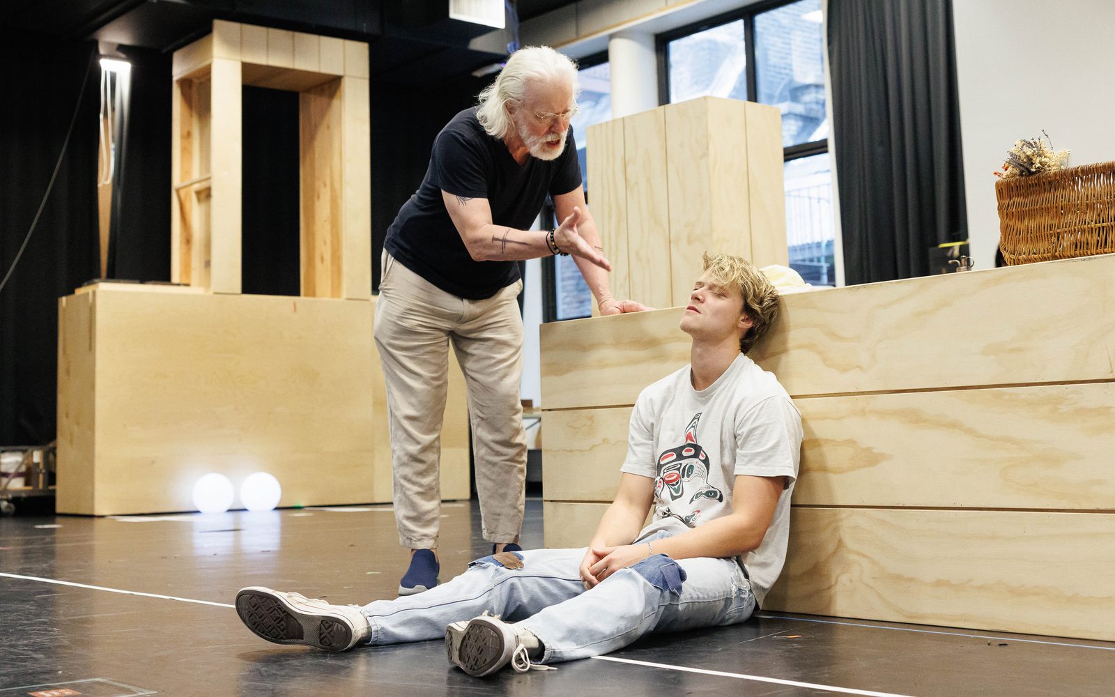 Terrence Mann leans over and gestures towards Rudy Pankow, seated on the floor.