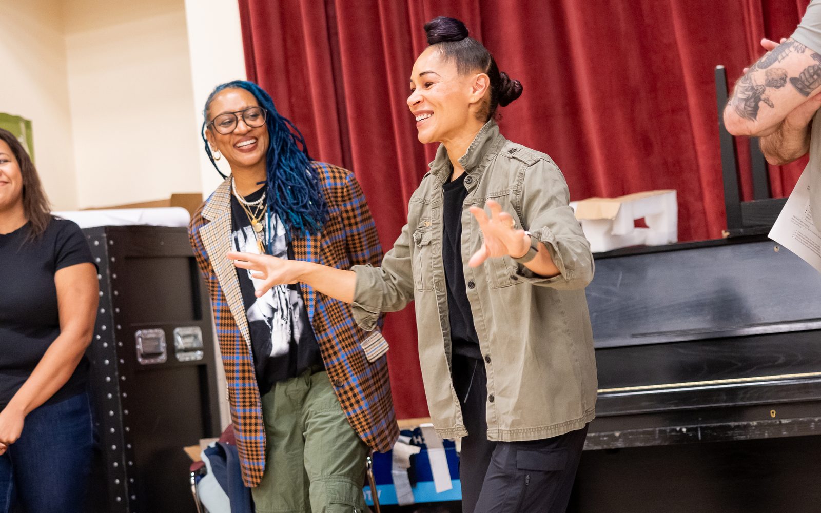 Ayodele Casel in a khaki jacket gestures with her hands while speaking, with Torya Beard in a bright plaid sport coat and graphic T-shirt stands next to her smiling.