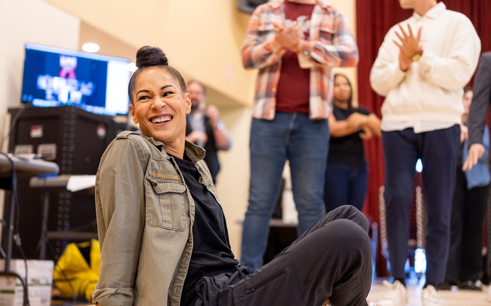 Ayodele Casel sits cross-legged on the ground smiling over her shoulder.