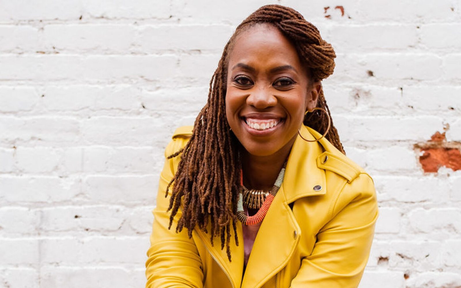 Quynn L. Johnson in a yellow leather jacket and with her braids falling over her shoulder smiles broadly.