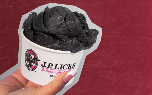 A hand with french tipped nails holds a J.P. Licks cup with a scoop of black ice cream in it.