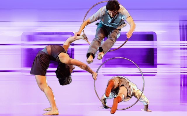 An acrobat holds out two hoops which performers jump through in opposite directions, against an illustration of a purple subway car speeding by.