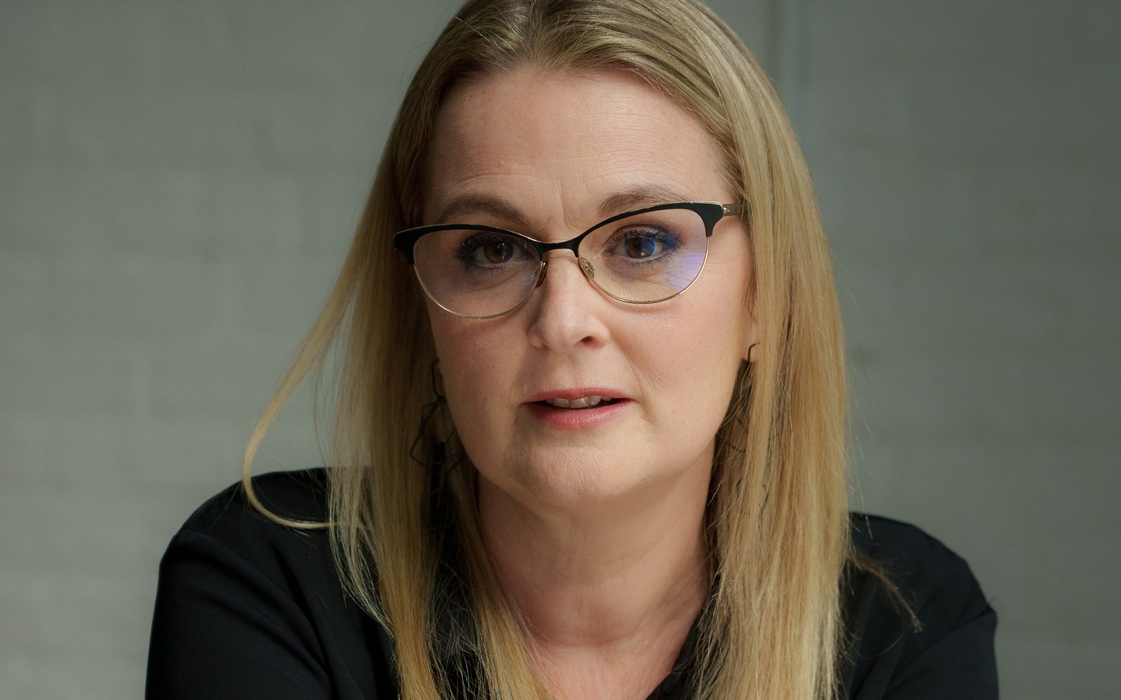 Closeup of Shana Carroll with blonde hair, black cat-eye glasses, and a muted pink lipstick.