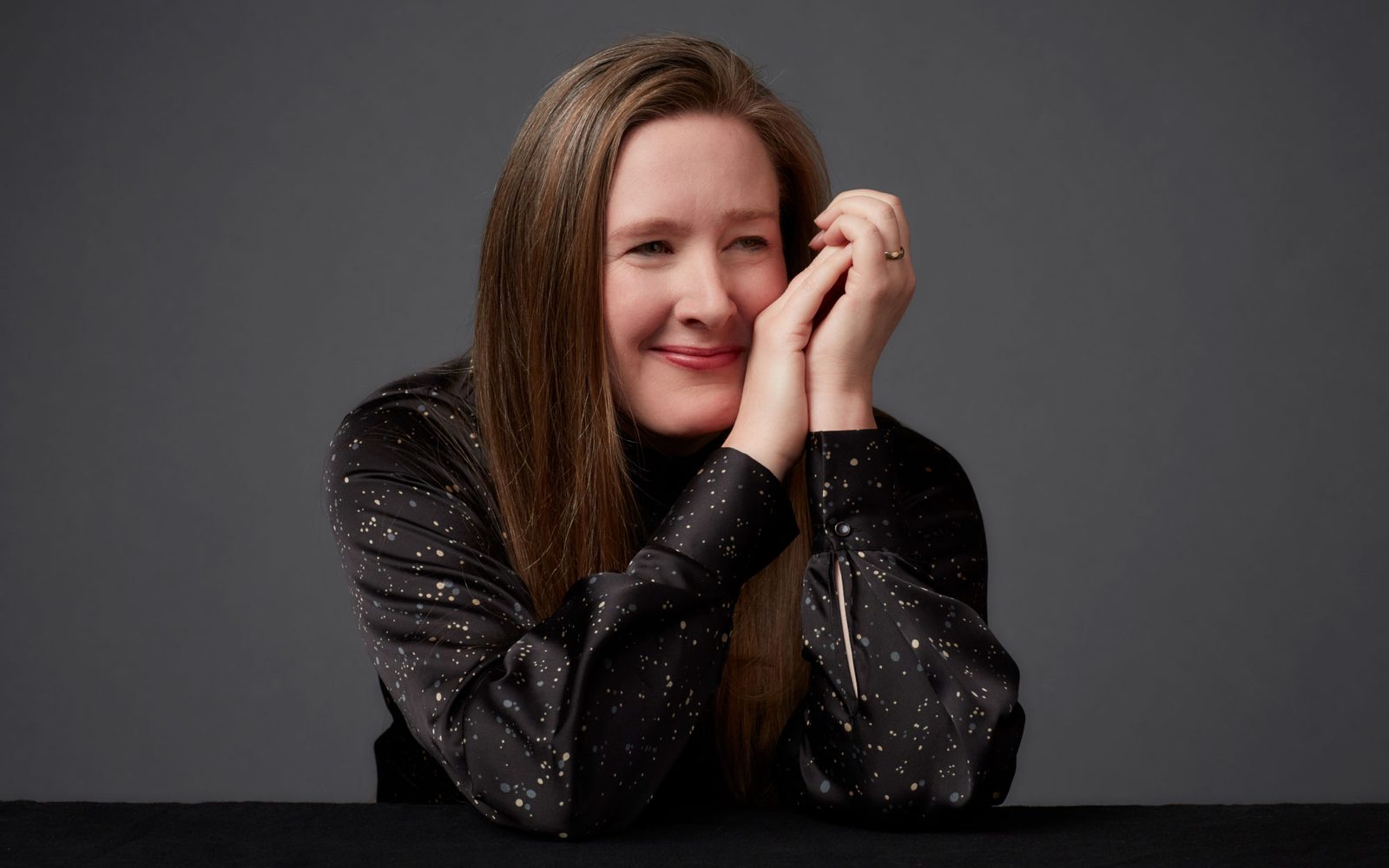 Sarah Ruhl in a sparkly black blouse clasps her hand in front of the left side of her face