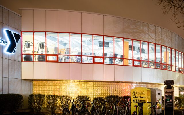 The exterior of the Roxbury YMCA, a curved building with full-length windows on the second floor, at night.