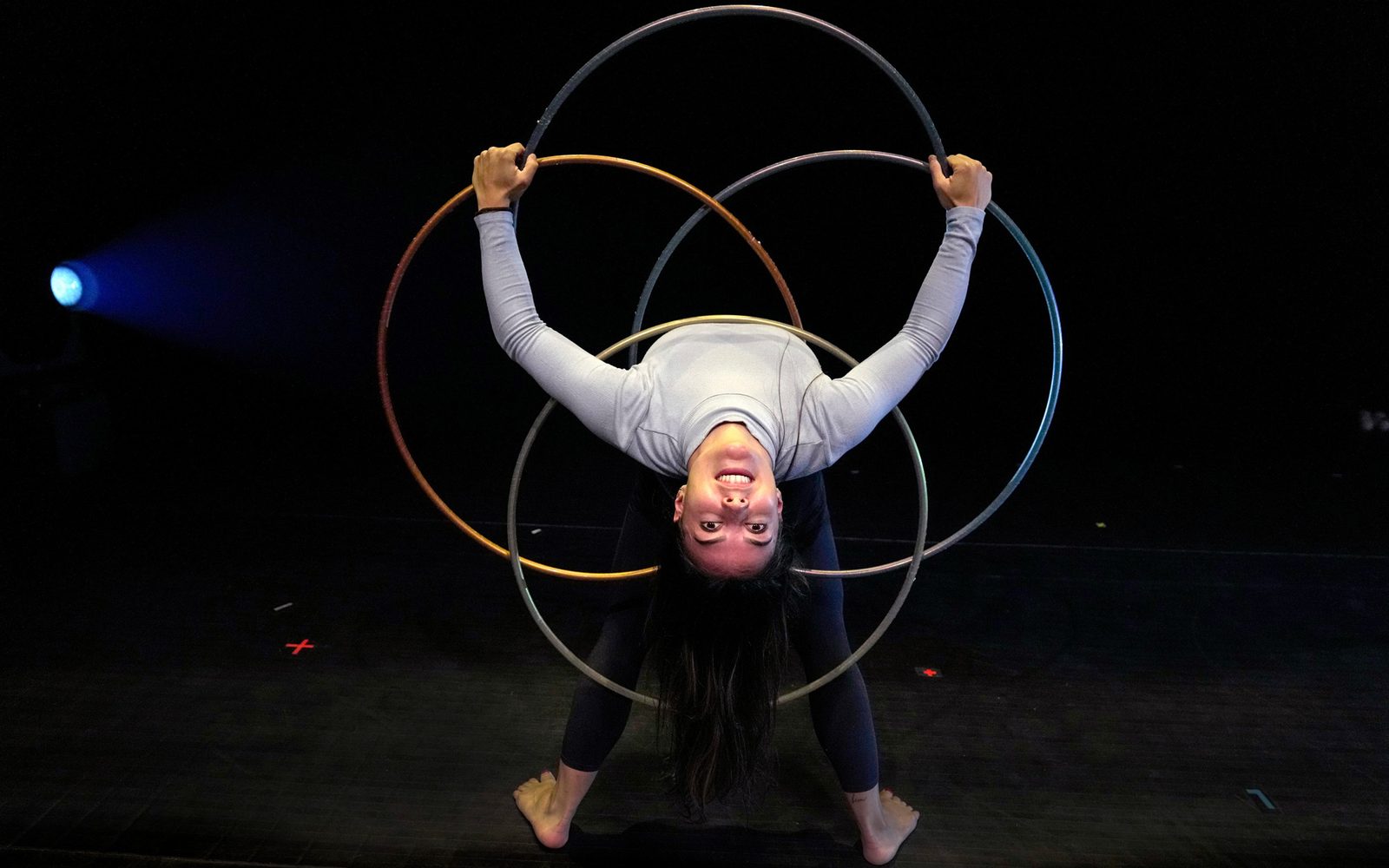 Méliejade Tremblay-Bouchard bends over backwards, holding up four hula hoops in a geometric configuration around her torso.