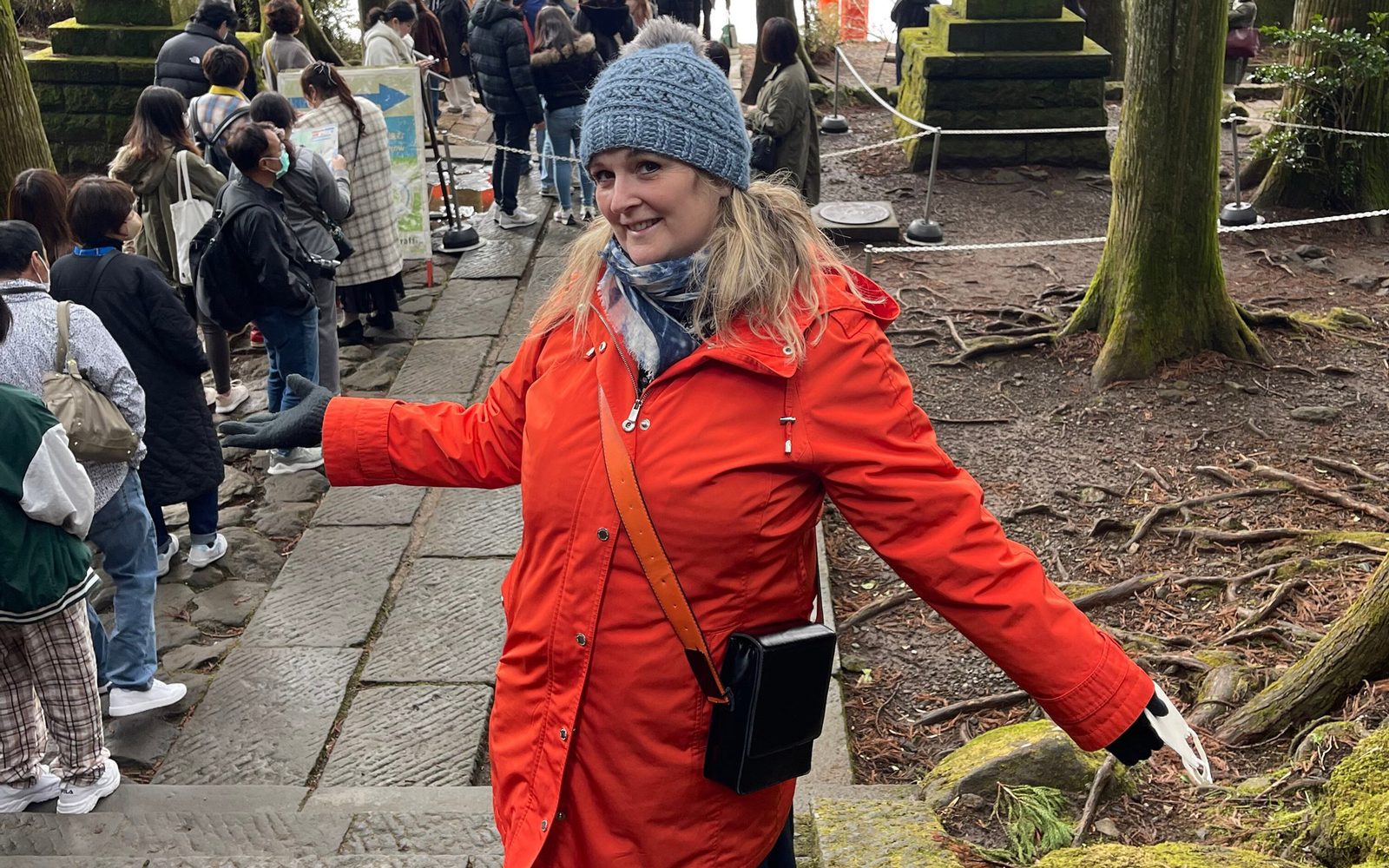 Shana Carroll in a knit cap and bright red winter jacket stands in front of a torii gate in Hakone, Japan.
